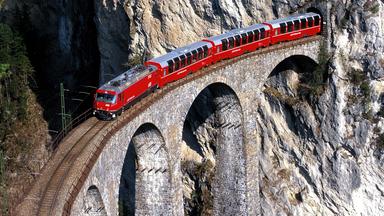Eine rote Eisenbahn zwischen steilen Felsen.