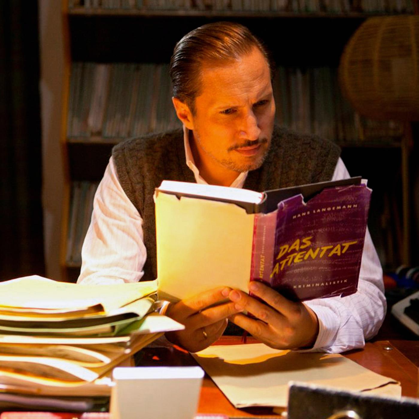 Ulrich Chaussy (Benno Fürmann) sitzt am Schreibtisch und liest das Buch "Das Attentat".