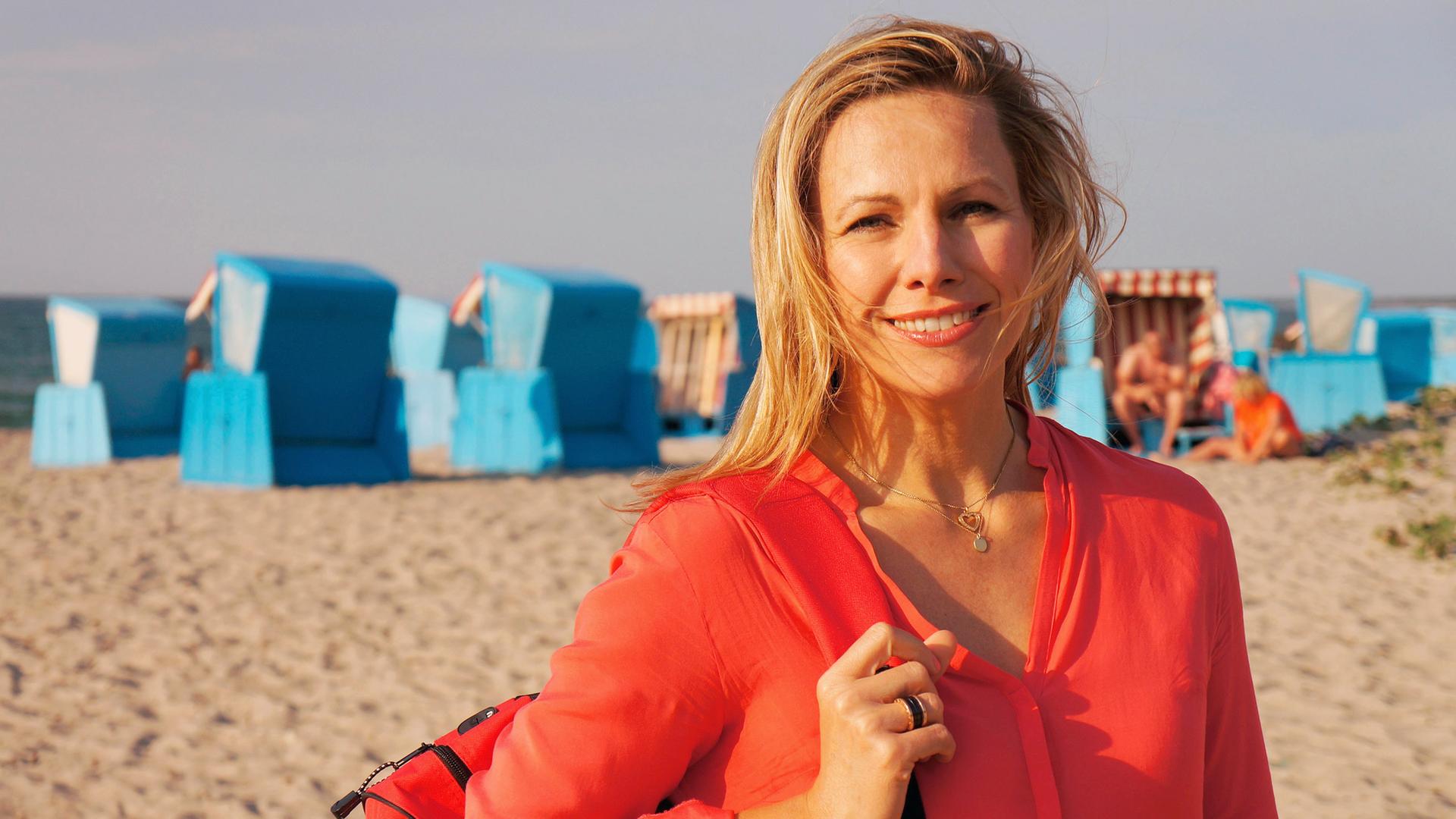 Porträt: Eine Frau steht am Strand, hinter ihr Strandkörbe.