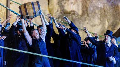 Gruppe von Sängern recken sich nach einem hochgehaltenen Fass