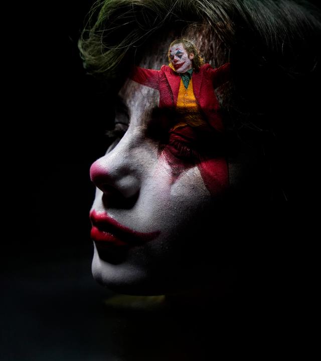 Nahaufnahme eines als Clown geschminkten Jungen. Sein Gesicht ist zur Hälfte im Dunkeln, auf seiner Stirn ist klein eine Szene des tanzenden Jokers eingeblendet.
