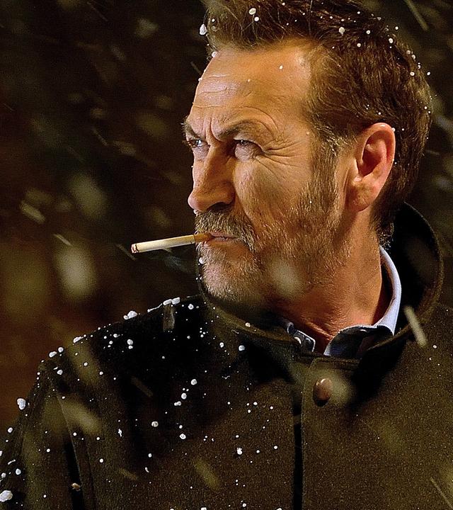 Kommissar Rocco Schiavone (Mario Giallini) steht mit einer Zigarette im Mund im Schneefall