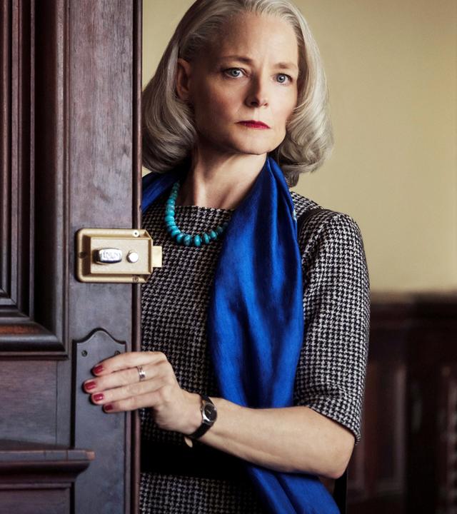 Eine Frau blickt hinter einer Tür hervor.