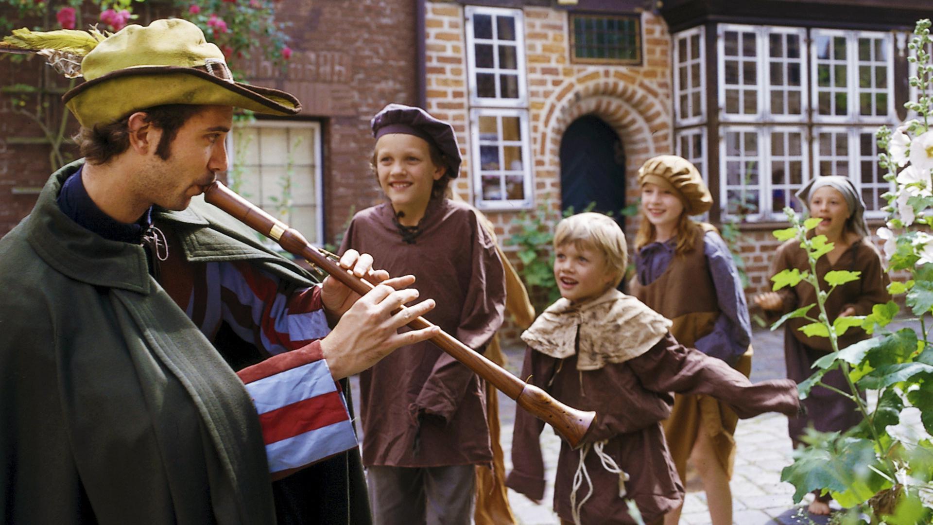 Der Rattenfänger bläst auf seiner Flöte und ein paar Kinder folgen ihm