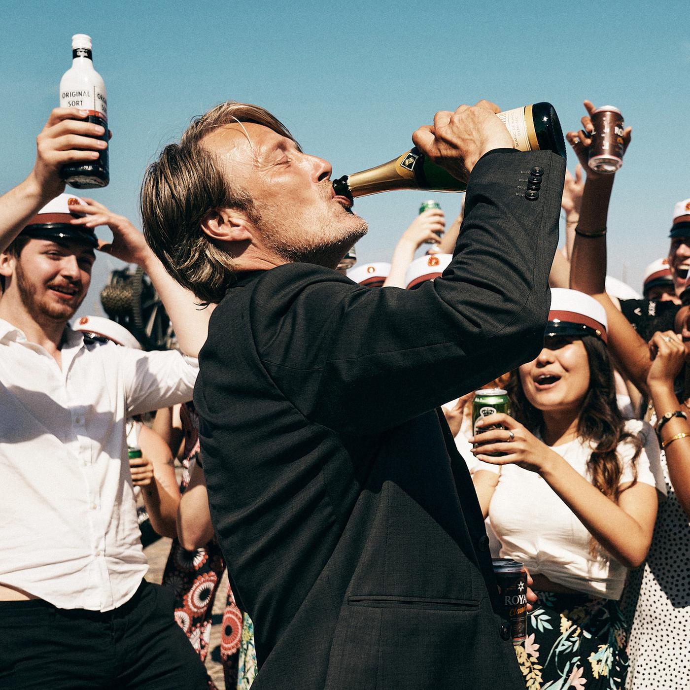 Ein Mann trinkt aus einer Flasche. Um ihn herum jubelnde dänische Schulabsolventen.