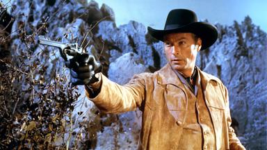 Dr. Karl Sternau (Lex Barker) steht in einer bergigen Landschaft und zielt mit erhobenem Arm mit einer Pistole auf ein Ziel außerhalb des Bildes.