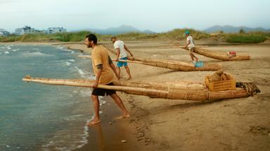 Drei peruanische Fischer ziehen ihre Schilfboote hinter sich her ins Meer.