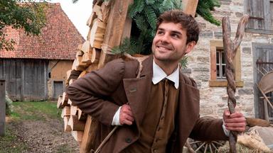 Ein junger Mann mit einer Trage voller Holz auf dem Rücken.