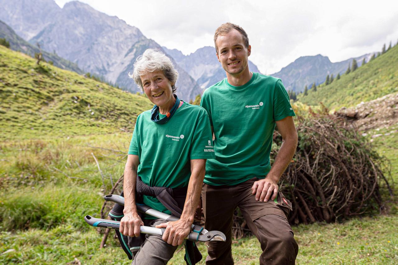 Zwei Angehörige des österreichischen Alpenvereins: Eine Frau mit einer Baumschere und ein junger Mann blicken lächelnd in die Kamera