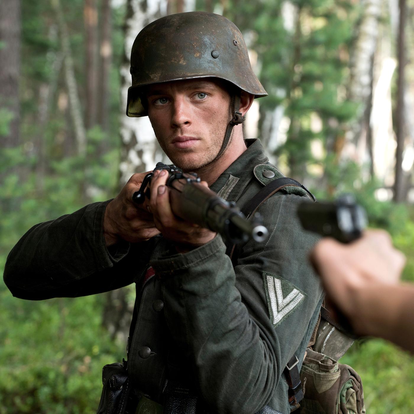 Walter Proska (Jannis Niewöhner) steht in Militäruniform und Gewehr im Wald und zielt auf eine Person, die eine Pistole auf ihn hält