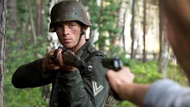 Walter Proska (Jannis Niewöhner) steht in Militäruniform und Gewehr im Wald und zielt auf eine Person, die eine Pistole auf ihn hält
