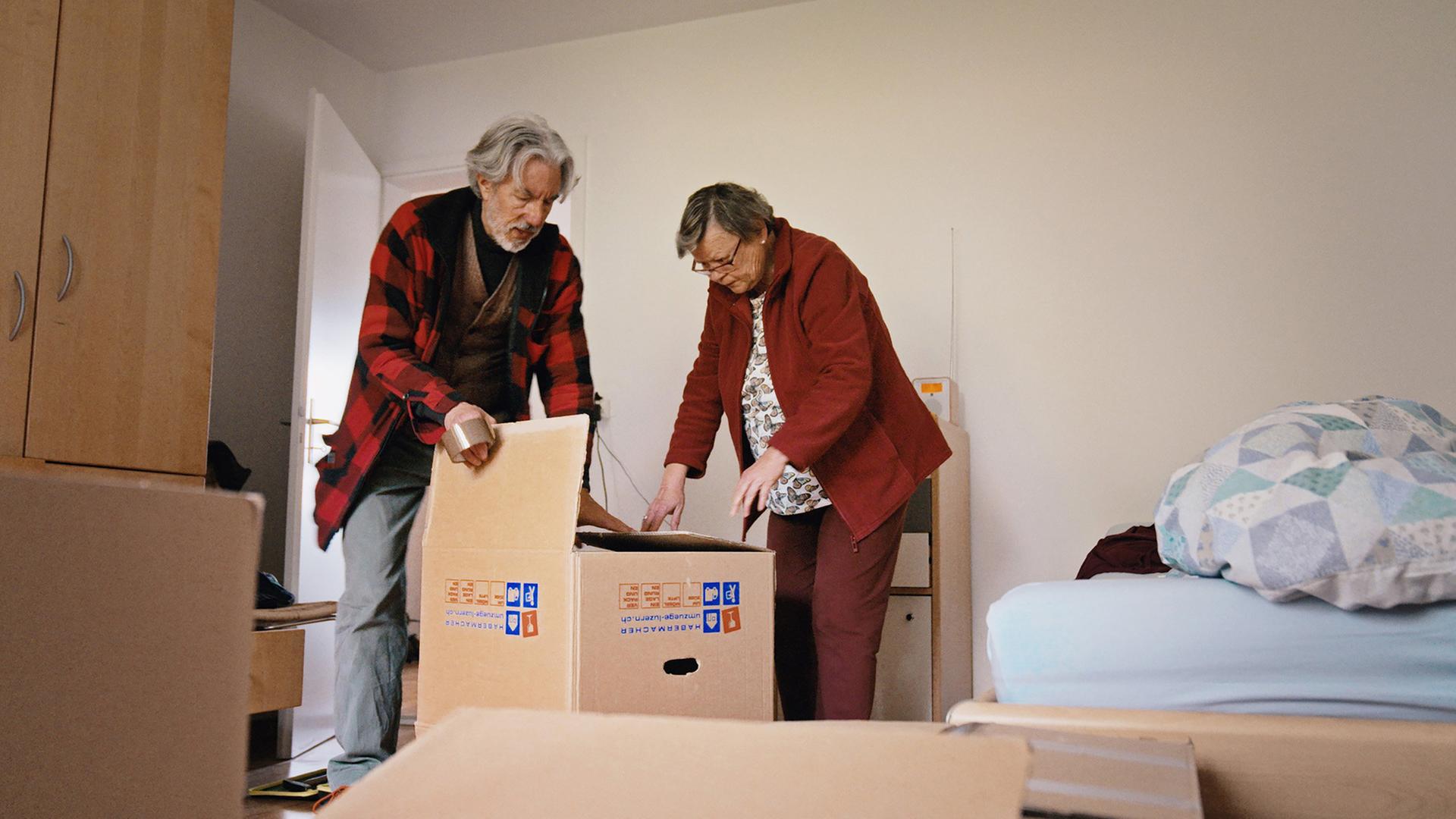 Zwei Männer stehen in einem Schlafzimmer und packen Umzugkartons