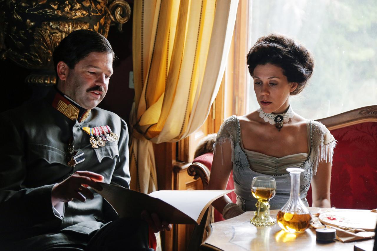 Ein Mann in Uniform und eine Frau in einem Kleid der Jahrhundertwende sitzen an einem Tisch 