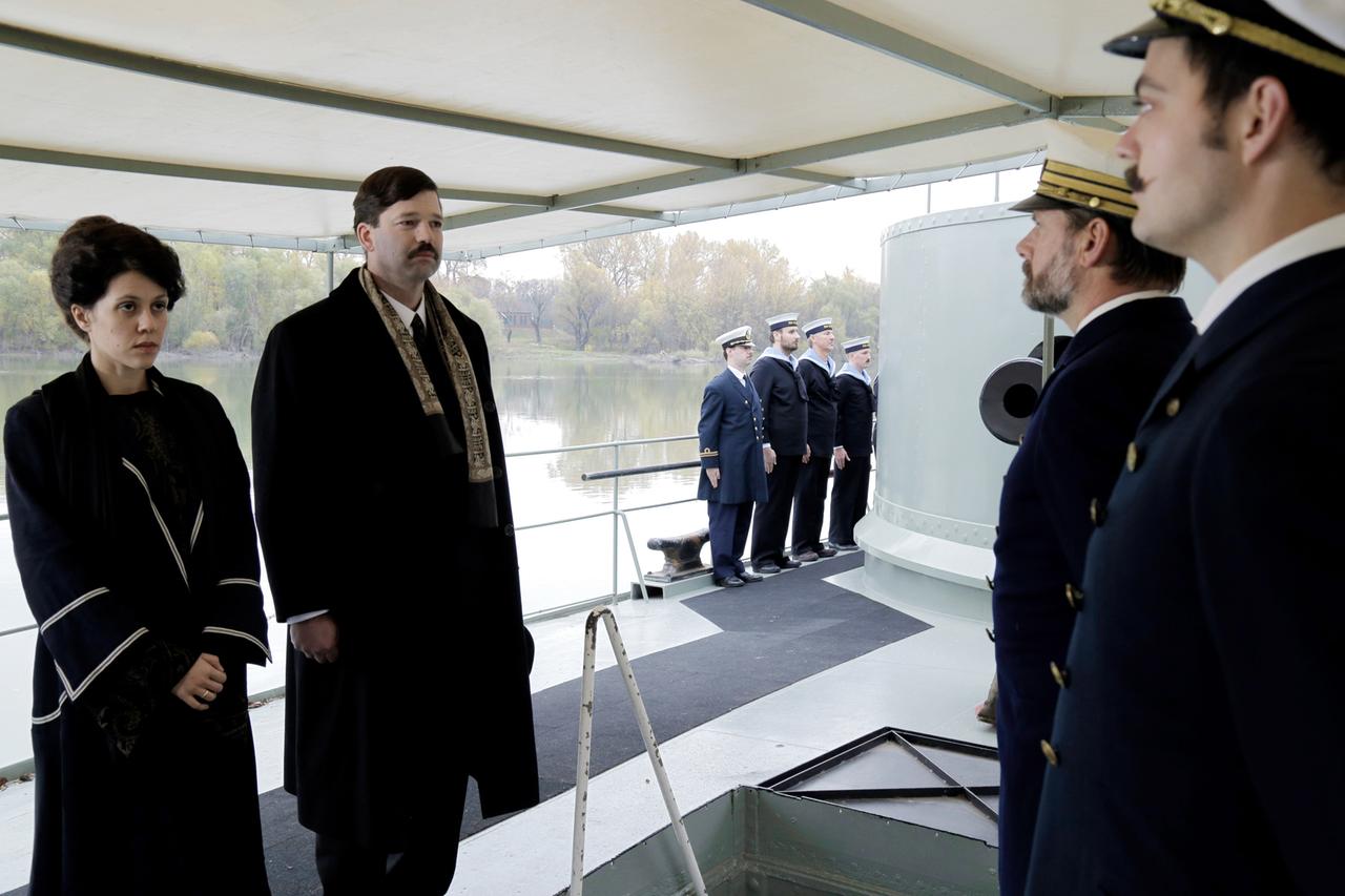 Ein Paar auf einem Schiff, schaut zum Kapitain und der Besatzung des Schiffes.
