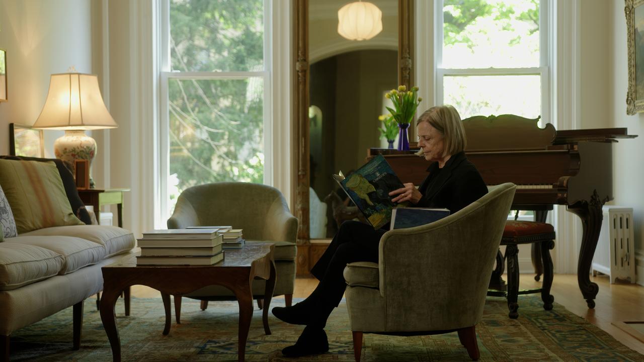 Frau in elegantem Biedermeier-Wohnzimmer mit Katalog des Aktionshauses "Christie's" in der Hand, auf dem das Portrait des Dr.Gachet auf der Titelseite zu sehen ist.