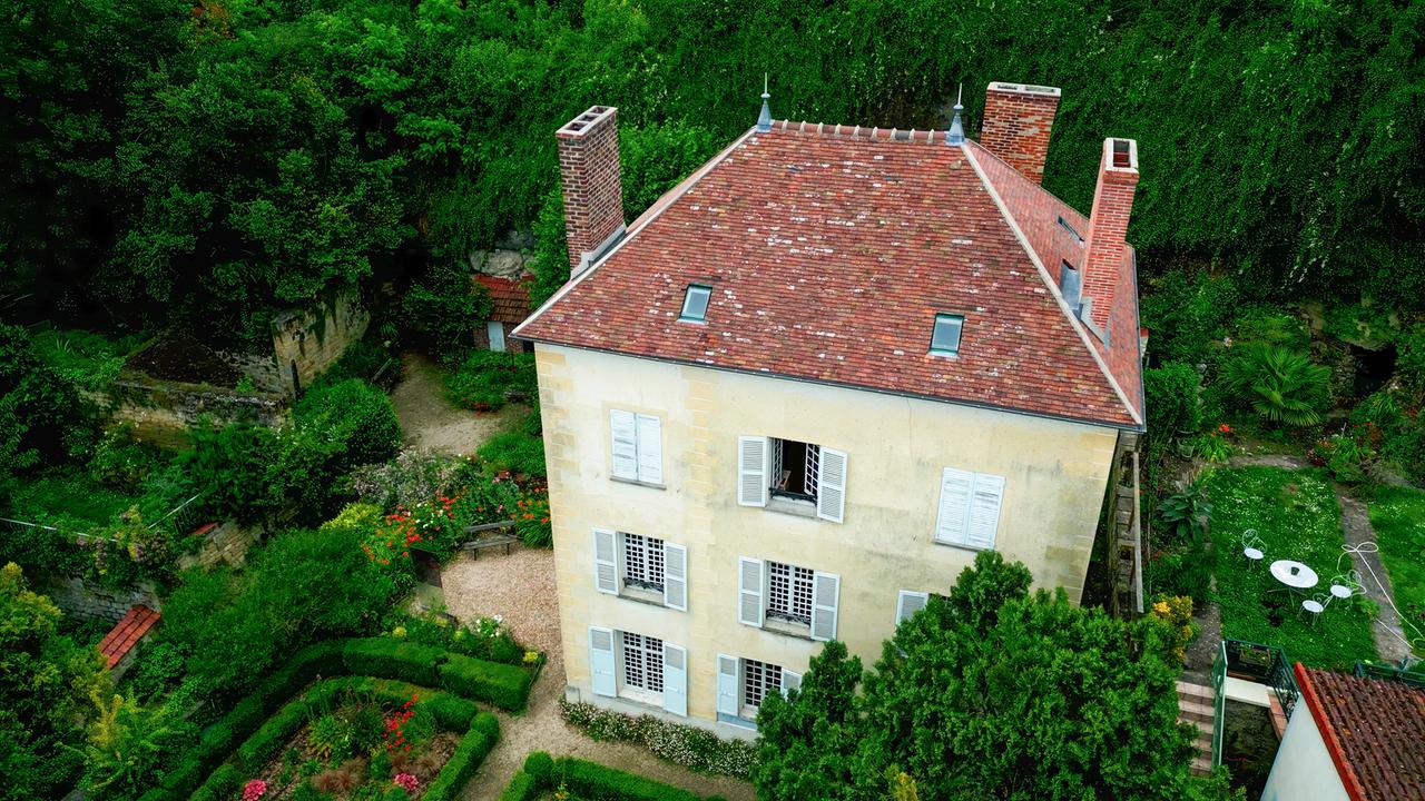 Dreistöckiges gelbes Haus mit rotem Dach, umgeben von einem grünen Garten.