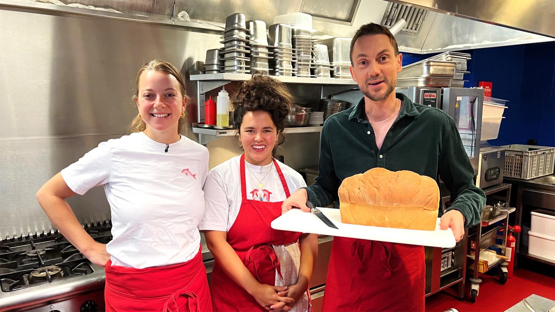 Drei Personen stehen in einer professionellen Küche und halten einen Kuchen