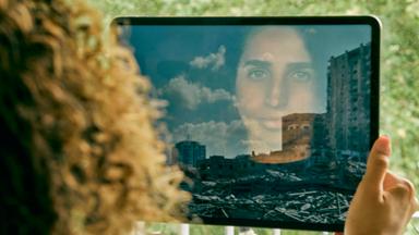 Das Gesicht von Darin Shammout (24) spiegelt sich in einem iPad. Auf dem ihr iPad ist ein Foto einer Trümmerlandschaft in der zerstörte Hochhäuser stehen.