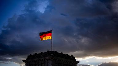Die deutsche Flagge auf einem Gebäude vor dem Hintergrund dunkler Wolken.
