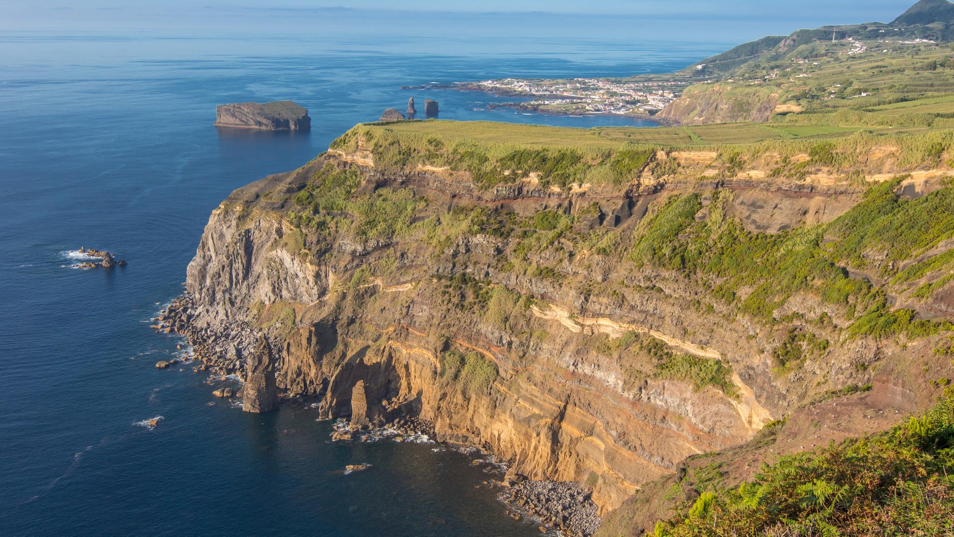 "Traumorte - Azoren": Grün bewachsene Felsenklippen vorm Meer.