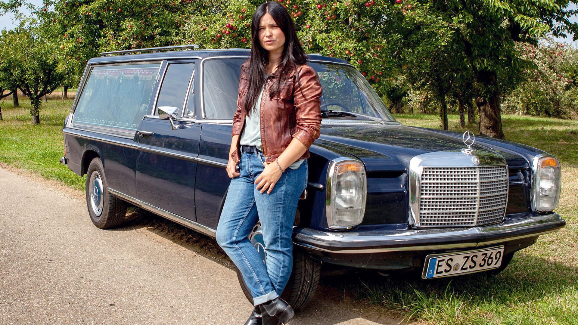 Junge Frau lehnt sich an ihren alten Mercedes.