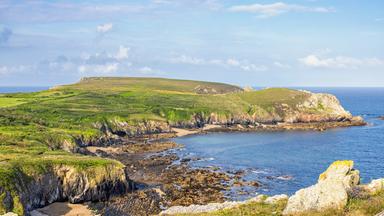 Blick auf die felsige Küste der Bretagne mit grünen Klippen, kleinen Buchten und dem Atlantik unter blauem Himmel.