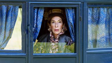 Eine Frau in edlen Klamotten blickt erschrocken aus dem Fenster einer Kutsche.