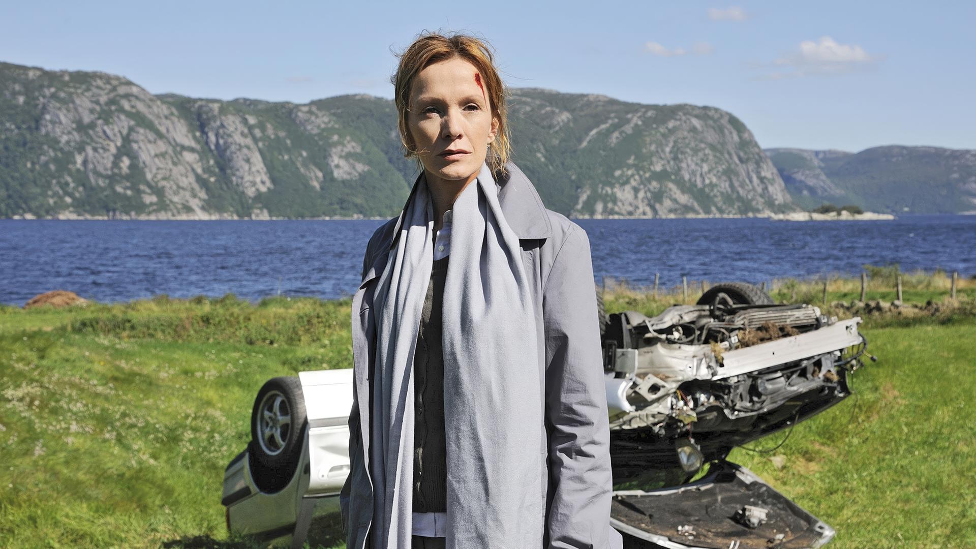 Eine Frau mit Platzwunde vor einem zerstörten Auto.