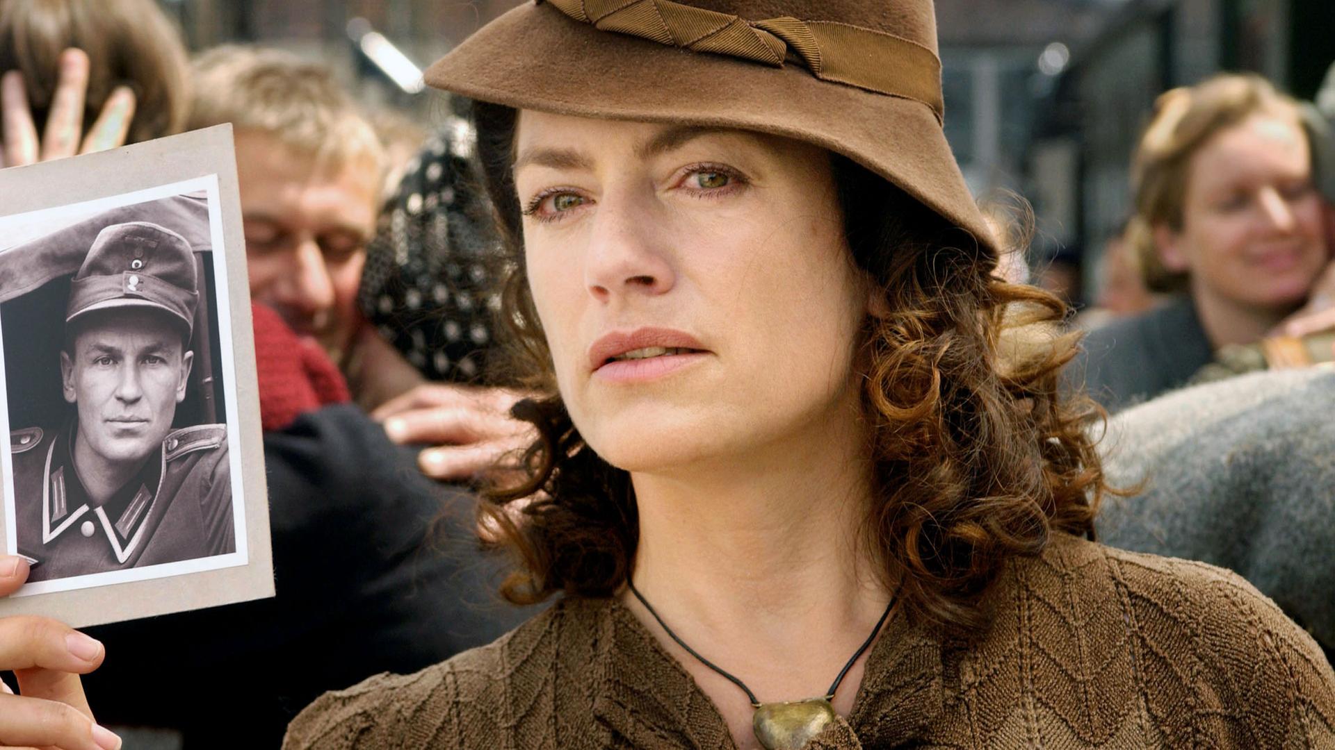 Eva (Christine Neubauer) steht am Bahnhof und hält ein Foto ihres vermissten Mannes hoch.