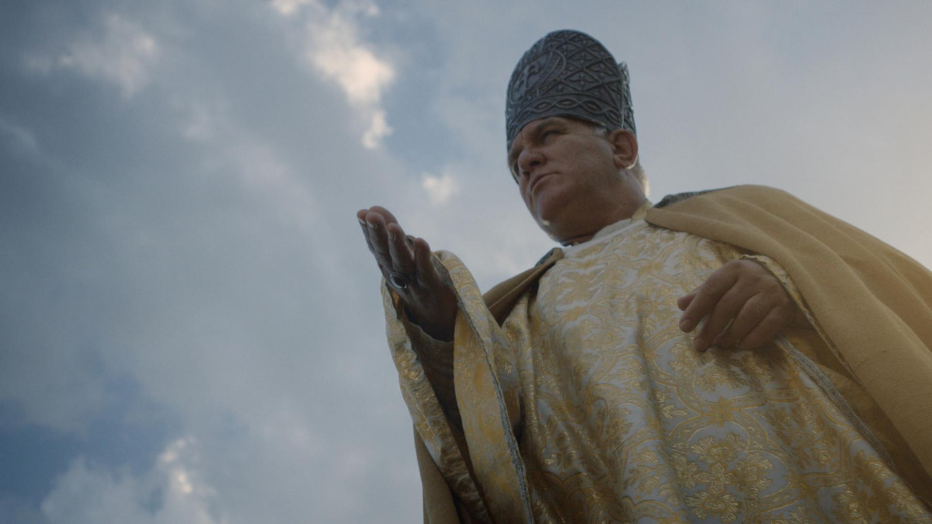 Ein Mann in der Kleidung eines Bischofs streckt verheißungsvoll die Hand aus.