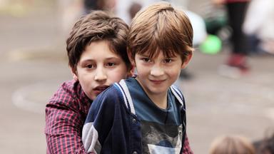 Zwei Jungen. Einer umarmt den anderen von hinten.