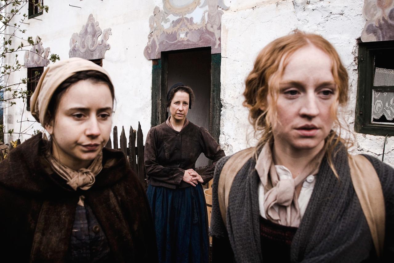 Zwei Frauen verlassen das Haus, eine Frau sieht ihnen nach.