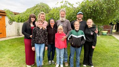 Mehrere Kinder und Erwachsene stehen zusammen auf einem Rasen vor einem niedrigen Baum