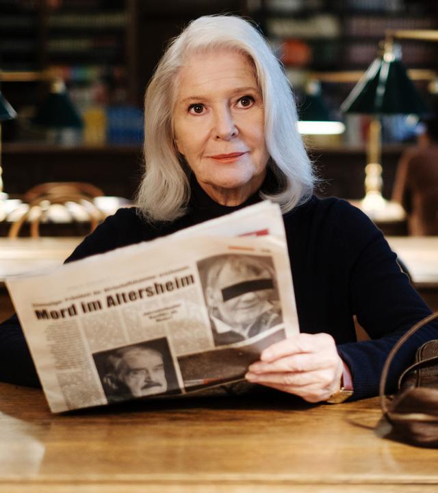 Eine Frau sitzt mit einer Zeitung in einer Bibliothek