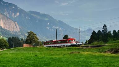 Eine Bahn auf Gleisen. Im Hintergrund Bergpanorama.