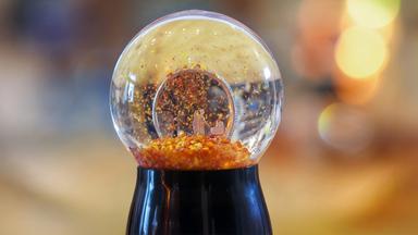 Eine Schneekugel, in der ein Pärchen zu sehen ist, das einen Kinderwagen im Herbstwald schiebt.