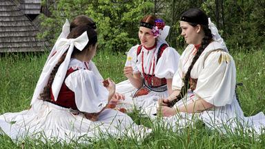 Märchen: Vier junge Frauen mit weißen Kleidern und Blumen und Schleifen im Haar sitzen in einer Wiese. 