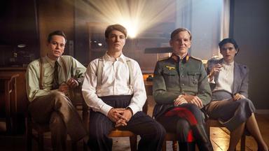 Drei junge Männer und eine junge Frau sitzen vor einem Projektor.