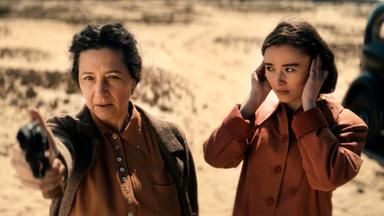 Eine Frau zielt mit einer Pistole. Daneben eine junge Frau.