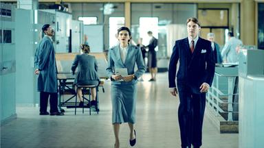 Ein junger Mann und eine junge Frau im Gang eines Bürogebäudes.