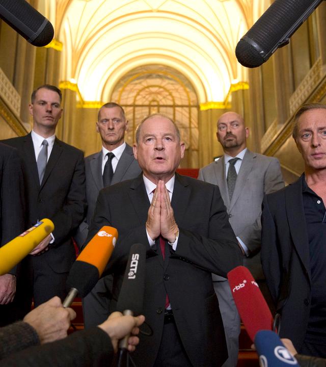 Sieben Männer umringt von Mikrofonen