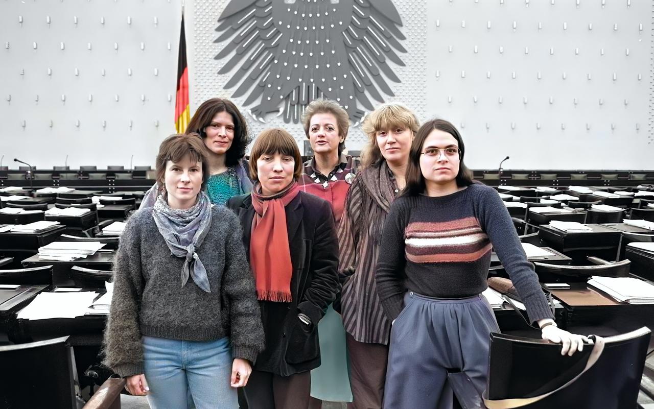 Koloriertes SW-Foto von 1984: eine Gruppe von sechs Frauen steht zusammen im leeren Plenarsaaldes deutschen Bundestages in Bonn.