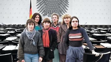 Koloriertes SW-Foto von 1984: eine Gruppe von sechs Frauen steht zusammen im leeren Plenarsaaldes deutschen Bundestages in Bonn.