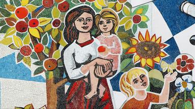 Mosaik mit einer Frau, die ein Kind im Arm hält, während ein weiteres Kind vor Blumen und einem Schmetterling steht; im Hintergrund ein Apfelbaum und Sonnenblumen.