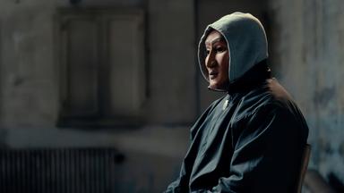 Eine maskierte Person sitzt auf einem Stuhl.