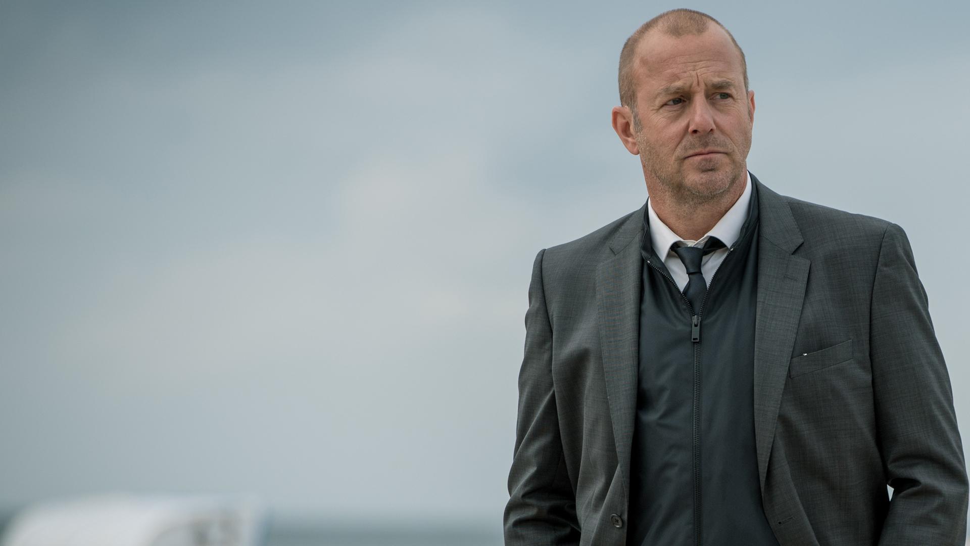 Kessler (Heino Ferch) steht am Strand. Im Hintergrund sind Strandkörbe zu erkennen.