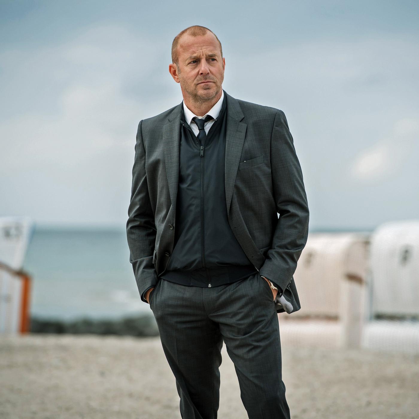 Kessler (Heino Ferch) steht am Strand. Im Hintergrund sind Strandkörbe zu erkennen
