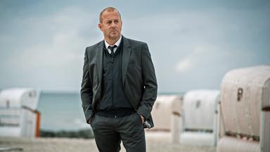 Kessler (Heino Ferch) steht am Strand. Im Hintergrund sind Strandkörbe zu erkennen