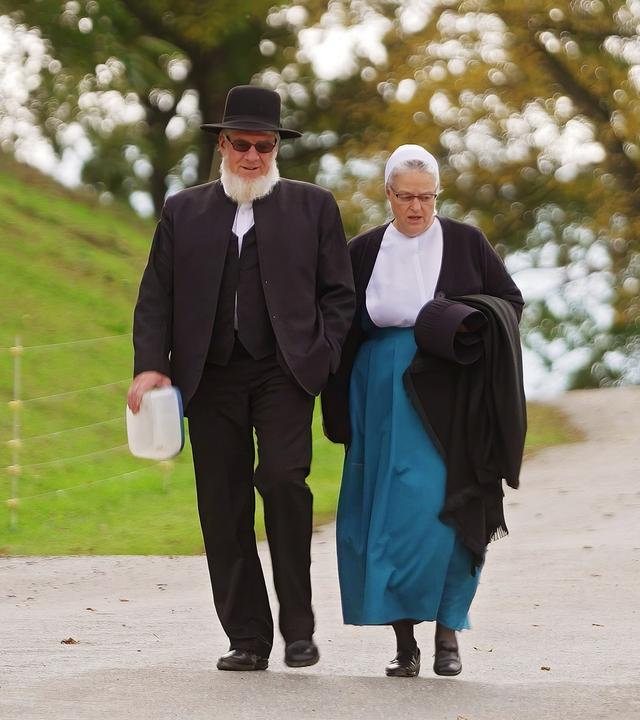 Ein älteres Paar in antiquierter Kleidung geht eine schmale Straße entlang.