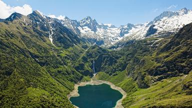 Blick auf einen idyllischen Gebirgssee, ringsum teils schneebedeckte Berge 